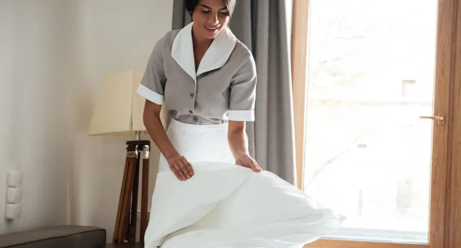 Maid-setting-up-white-bed-sheet-in-hotel-room