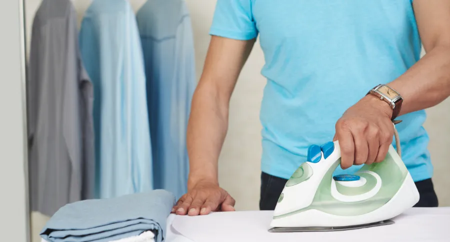 Unrecognizable man ironing shirts and laundry at home